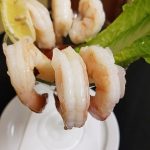 Shrimp cocktail with lemon wedge at Augie’s, served in a glass on a white plate with lettuce.