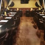 Empty restaurant at Augie’s with dark wooden tables, white napkins, and curtains at the back.