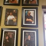 Framed photos of people at Augie’s hanging on a tan wall near a window.