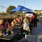 People enjoying outdoor dining at Augie’s under blue umbrellas on a sunny Prescott day.