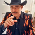 Man in a black cowboy hat and flame jacket smiles at Steakhouse Prescott’s outdoor dining area.