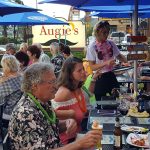 People dining outdoors at Restaurants in Prescott, with a waitress serving under blue umbrellas.