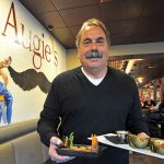Man with a mustache holding food trays inside Augies, one of the top restaurants in Prescott.
