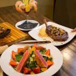 A table at Augie’s with salad, grilled steak, shrimp cocktail, and another steak on a wooden board.