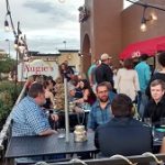 A busy outdoor patio at Augie’s, where guests dine and socialize under glowing string lights.