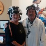 Two people in costumes with black and white wigs, smiling at Augie’s Cocktail Lounge indoors.