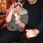 Woman in striped shirt with fake mustache enjoys wine at Cocktail Lounge, man beside her.