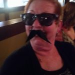 Woman in sunglasses and fake mustache smiles indoors at Augie’s, with banquet rooms in Prescott.
