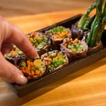 A hand picking up a veggie sushi roll in a cozy Steakhouse Prescott setting.