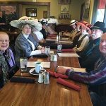 People in vintage clothing and hats smile at a long Steakhouse Prescott banquet table.