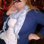 Woman in a blue cardigan poses with a fake mustache at an outdoor dining Prescott spot.