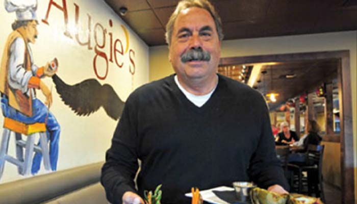 Man with a mustache enjoying food at a steakhouse in Prescott, mural brightening the scene.