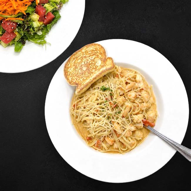 Plate of creamy pasta at Augie’s with toast and fork, salad partially visible on the side.