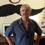 Older man with a mustache stands by a painted mustache at a classic steakhouse in Prescott.